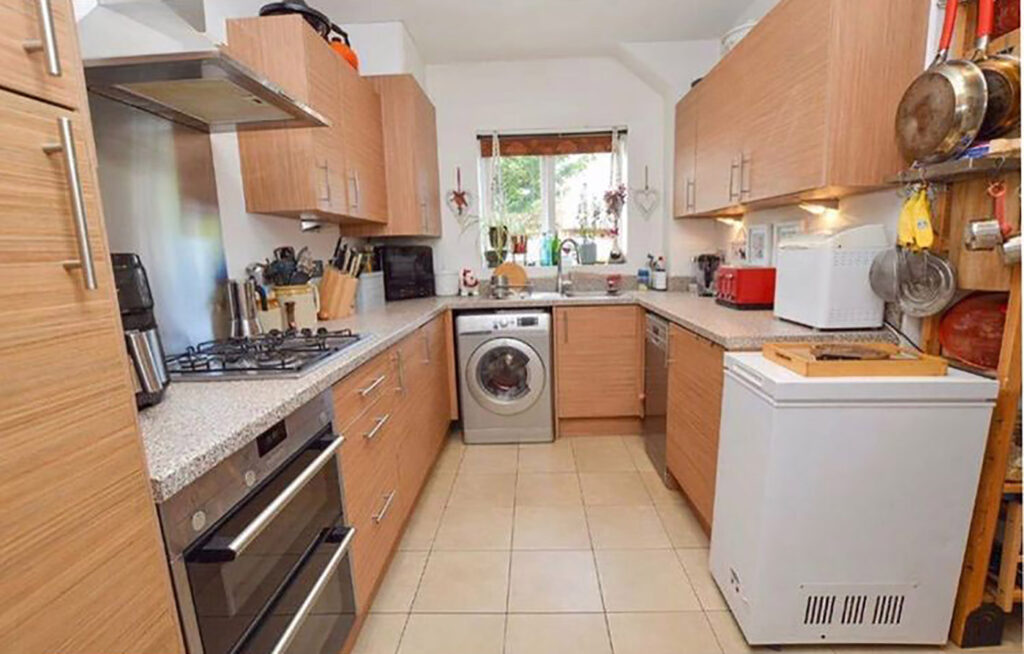 The kitchen before with wooden cabinets, yellow tinted tiling and clunky appliances.