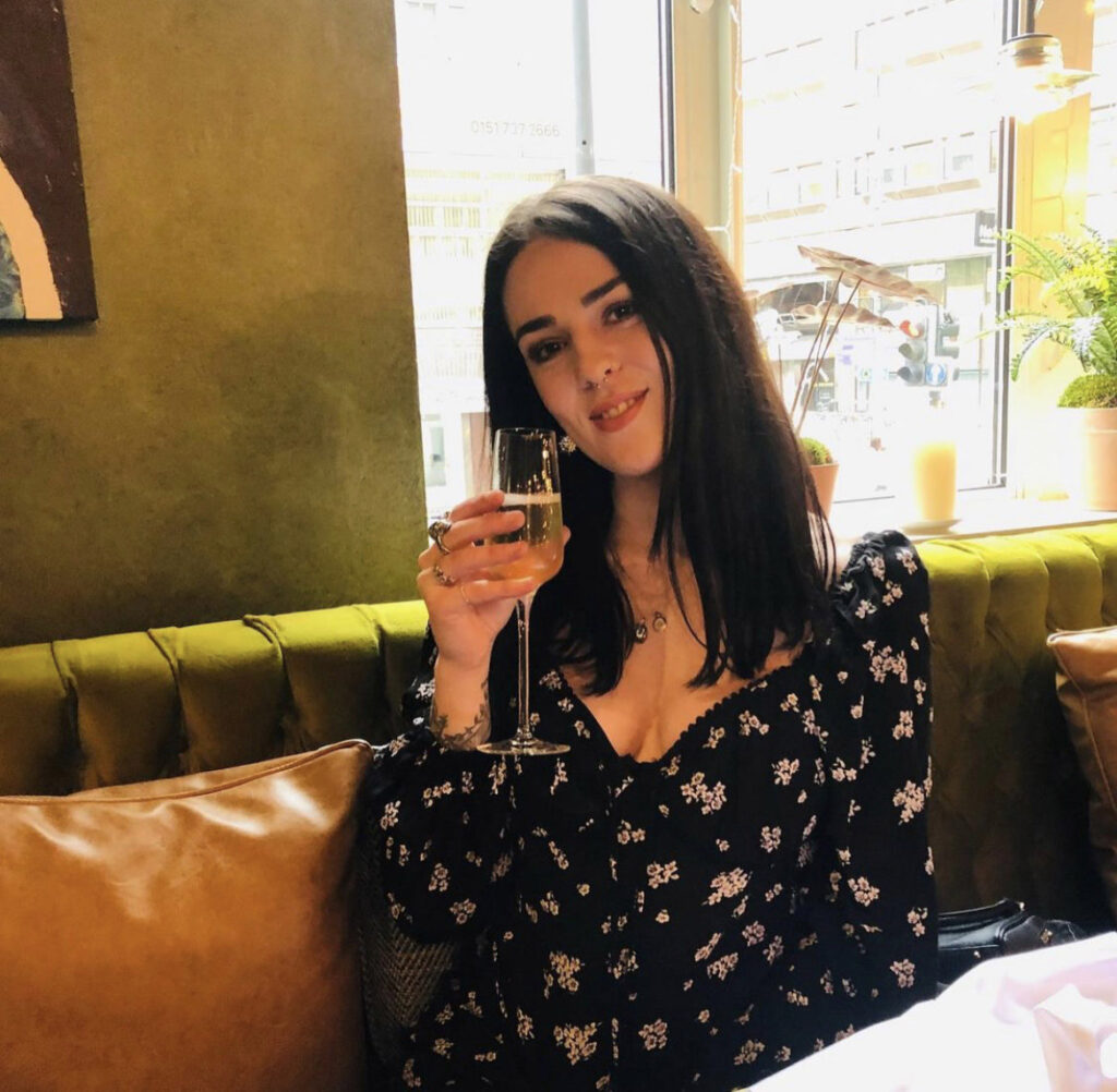 Sophie wearing a dress and smiling while holding up a glass of fizz
