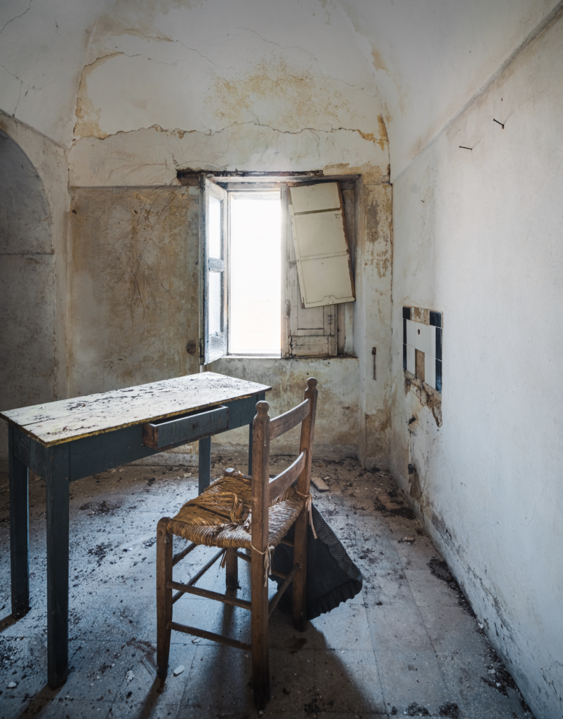A chair sits alone next to a wooden table in a room with cracked walls. 
