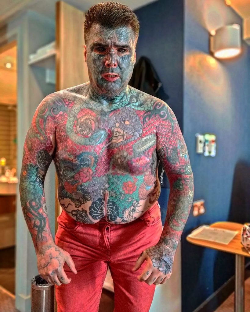 King Of Ink Land poses with his top off and red tourers as he looked into the camera with his tattoos. 