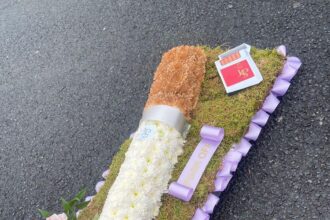 Florist's cheeky cigarette-shaped funeral display with a 'f**k off' ribbon goes viral. Made by Beaukays Bespoke Flowers in Liverpool, it honors a woman who loved cigarettes and telling people off. Social media users joke about similarities to famous smokers like Eastenders' Dot Cotton and Benidorm's Madge Harvey.