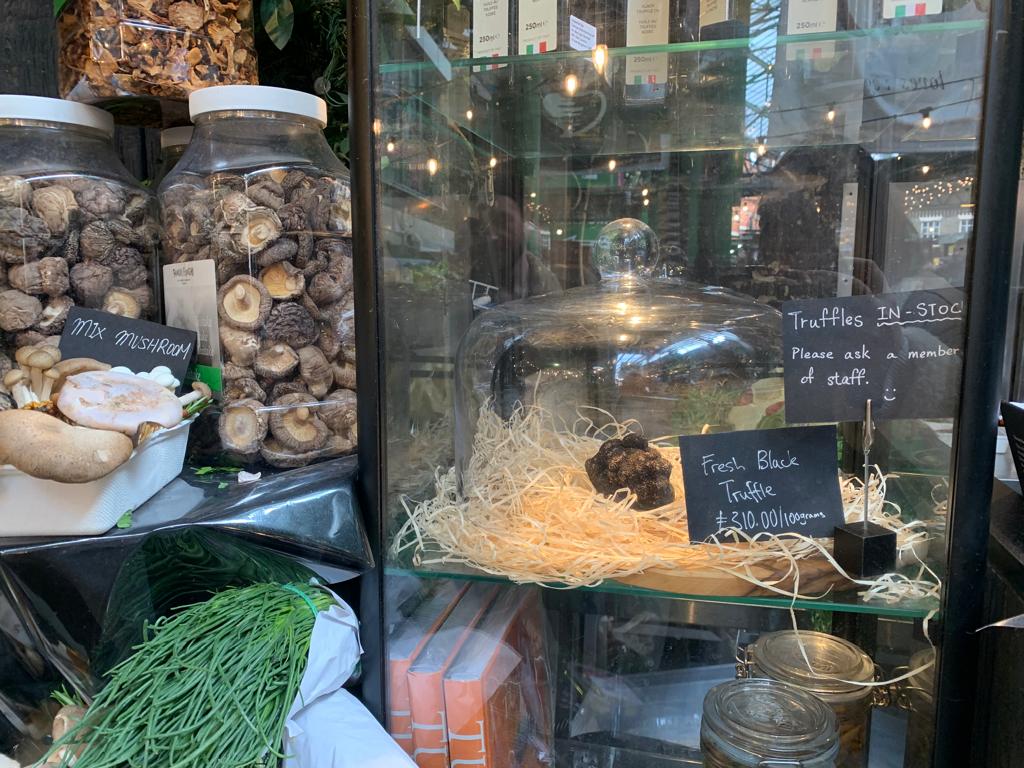 At a London food market, a rare black truffle fetches a hefty price of £310 per 100 grams, leaving shoppers astonished at its luxury.