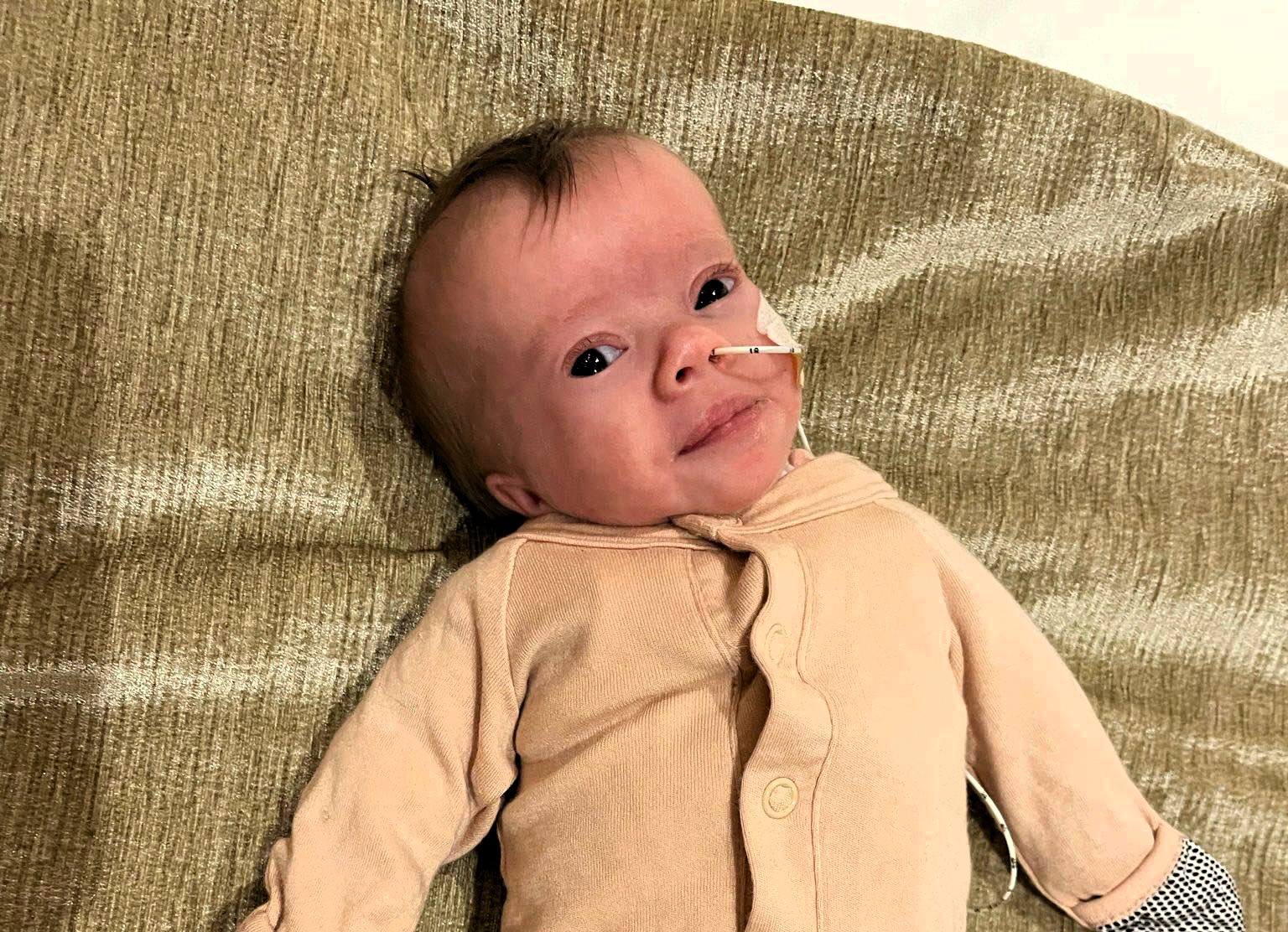 A tiny fighter, Nora, born weighing just 1lb 2oz, battles her rare condition with a contagious smile. Her parents share her feeding tube journey and resilience.