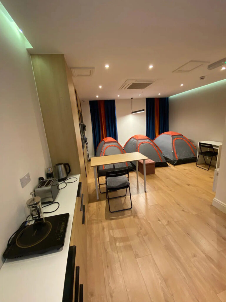 The viral Airbnb listing, infamous for renting tents in a London flat's living room, has resurfaced with a higher price tag of £80 per night. Despite the unconventional accommodations and potential noise, amenities like a shared kitchen and bathroom are provided.