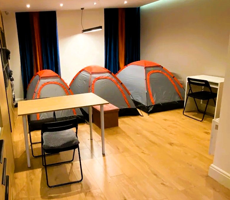 The viral Airbnb listing, infamous for renting tents in a London flat's living room, has resurfaced with a higher price tag of £80 per night. Despite the unconventional accommodations and potential noise, amenities like a shared kitchen and bathroom are provided.