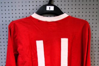 George Best's 1967-68 Manchester United shirt, worn during his peak season, sells for £13,300 despite a hole. Includes match programs, shorts, and memorabilia from his career.