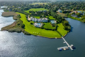 Luxury Hamptons compound with 24 bedrooms, 38 bathrooms, indoor basketball court, and 750-gallon shark tank listed for £77.8m ($99.5M). Stunning ocean views and amenities.