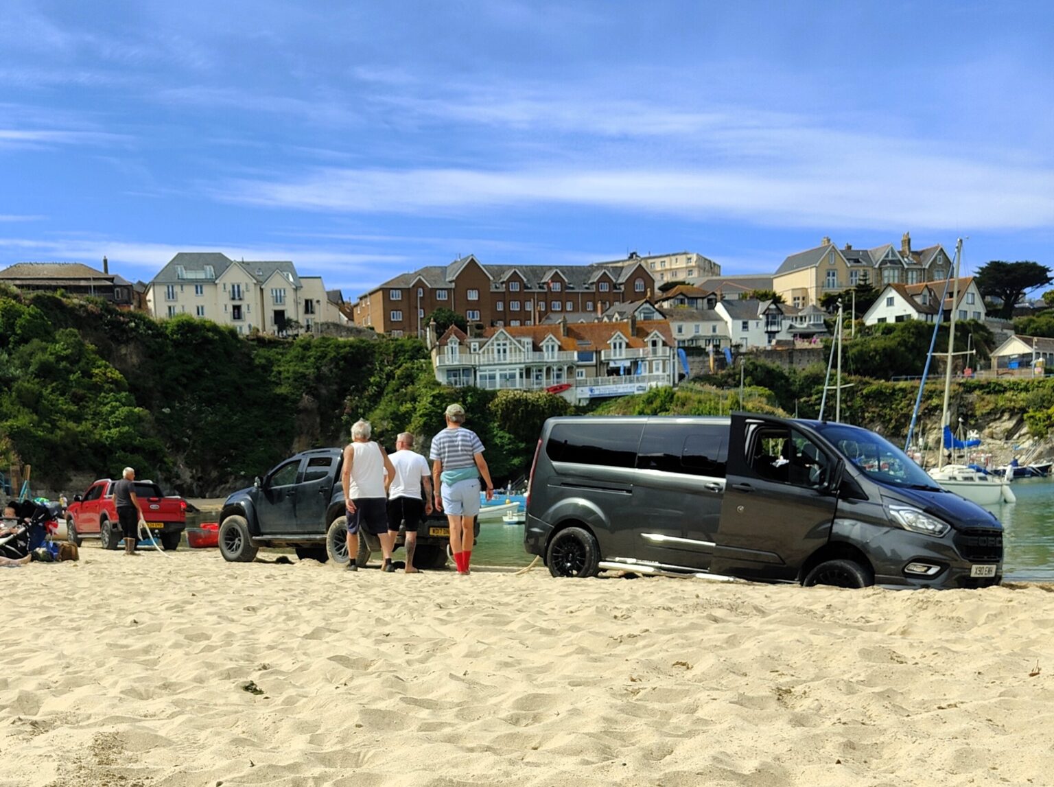 Tourist gets minivan stuck on Newquay beach, requiring rescue by locals. Cornwall's "idiot summer" begins as more cars get stranded on beaches, amusing locals.