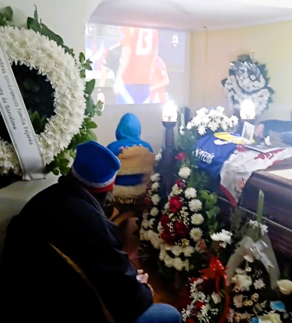 Mourners watch a live football match next to Grandpa Feña's open coffin at his wake in Chile. The passionate sports fan's funeral coincided with the Copa America.