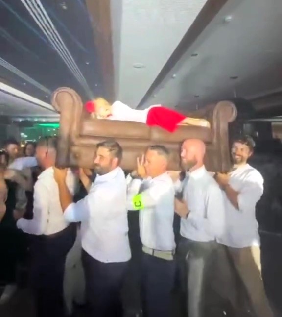 A sleepy wedding guest hilariously wakes up on a dance floor sofa carried by fellow guests. The viral video shows her bewildered reaction before nodding off again.