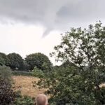 Sinister funnel cloud forms over Porthpean, Cornwall, causing alarm. This dramatic weather event resembles a tornado but doesn’t touch the ground. Witnesses react in fear.