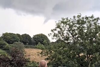 Sinister funnel cloud forms over Porthpean, Cornwall, causing alarm. This dramatic weather event resembles a tornado but doesn’t touch the ground. Witnesses react in fear.