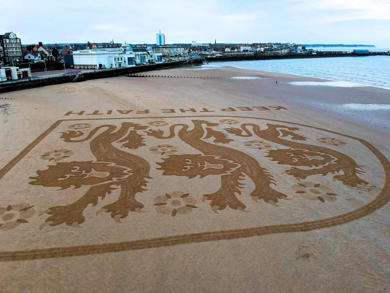 Artist Fred Brown created a huge England football badge on Bridlington beach to inspire Euro 2024 stars, captured by drone before the tide swept it away.