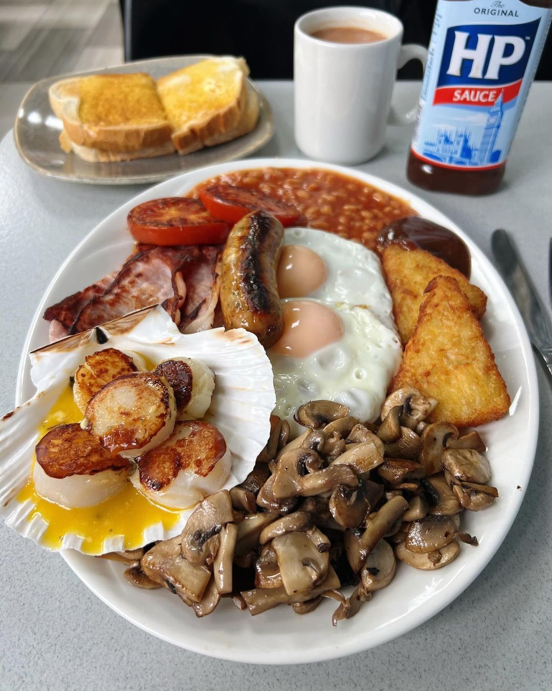 Diehard fry-up fans criticize Billingsgate Cafe's Full English breakfast with scallops, sparking debate over the unique £13 dish featuring traditional items and scallops in garlic butter.