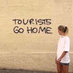 A tourist sparks online debate by sarcastically thanking Barcelona for a "warm welcome" beside a "tourists go home" sign, highlighting tensions over mass tourism in the city.