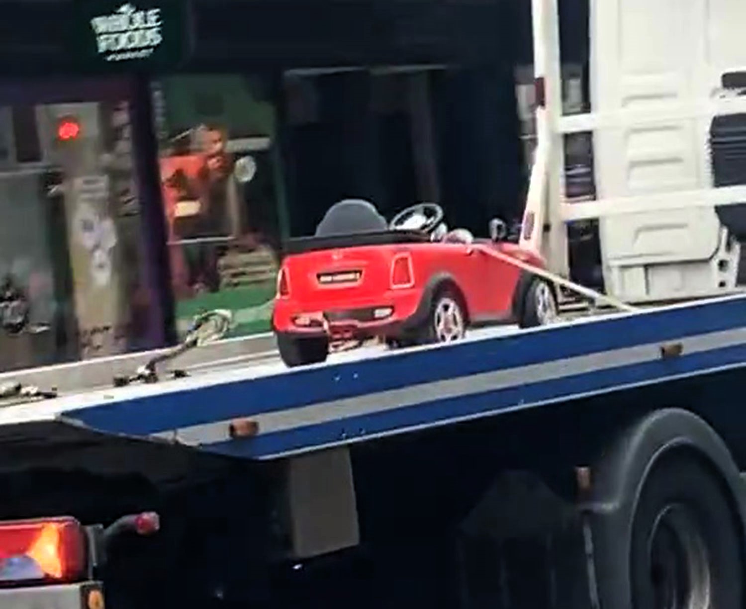 Toy Mini Cooper towed on flatbed in London, sparking jokes about the child owner's 'illegal parking' for sweets. Locals poke fun at the bizarre scene.