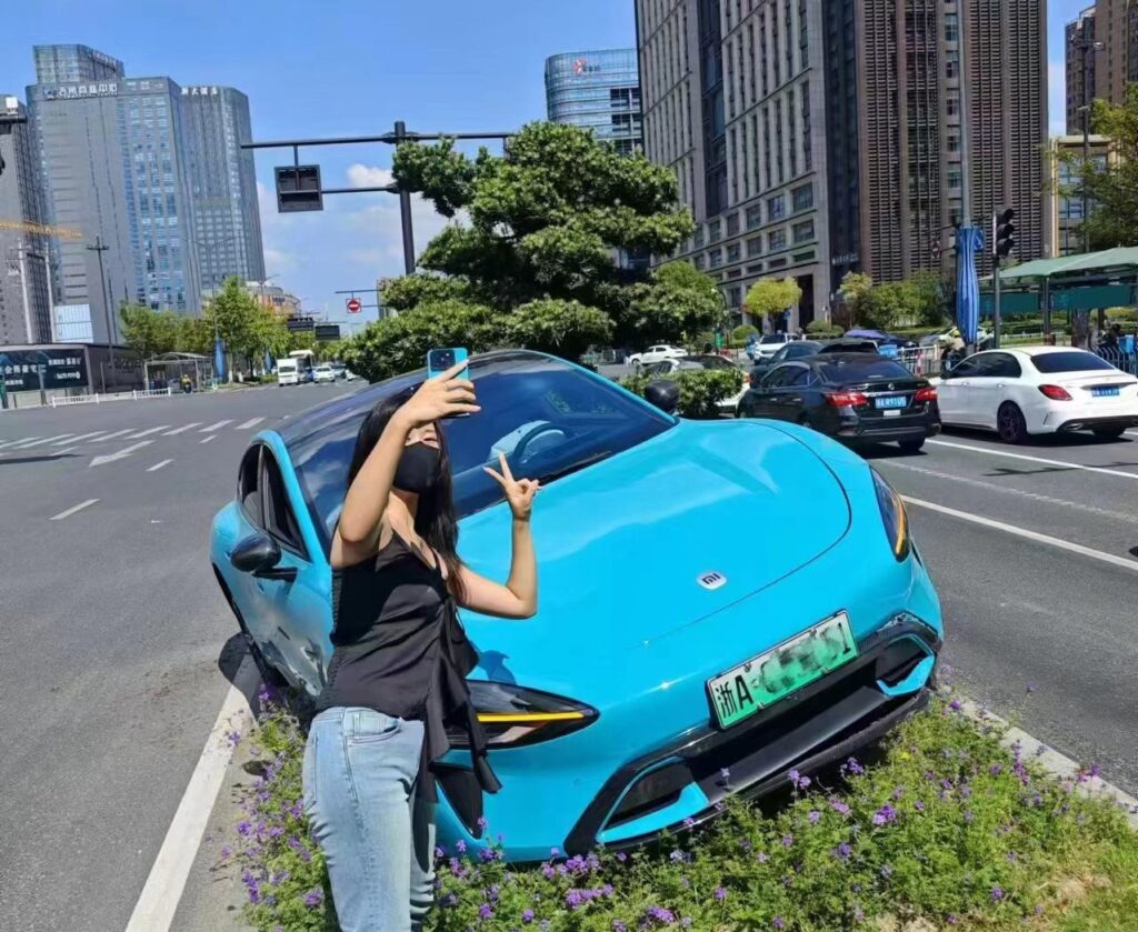 A woman took grinning selfies beside her crashed electric car after losing control and flattening a flowerbed, sparking debate online over her surprising reaction.