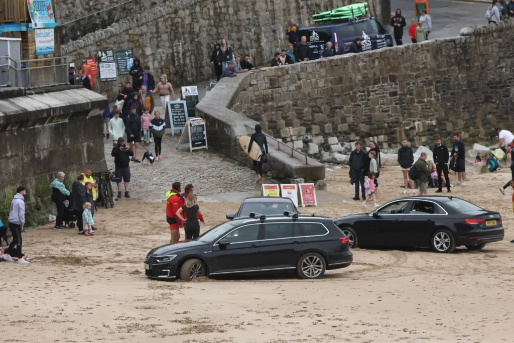 A tourist van got stuck on Polzeath beach in Cornwall as high tide approached, continuing the trend of “idiot season” incidents, with locals rushing to help free the vehicle.