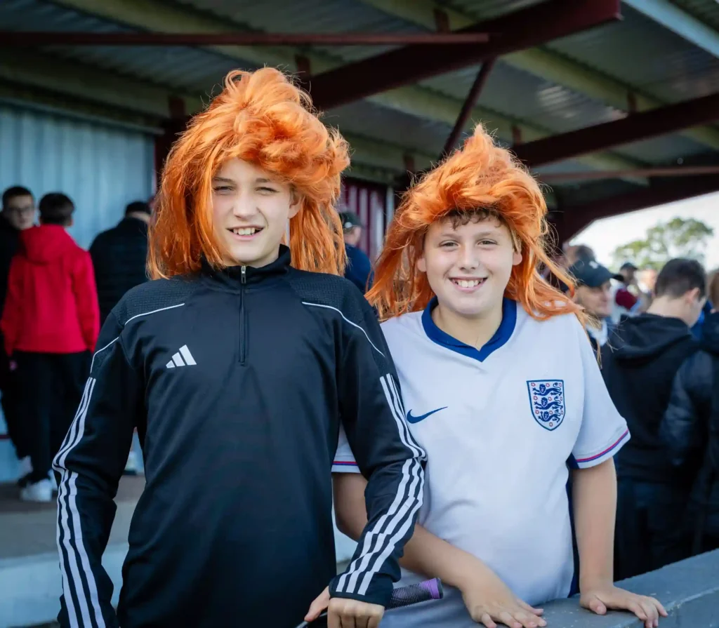 Taunton Town FC fans sport ginger mullet wigs in support of captain Tom Smith, sparking a booming trend at matches. The quirky craze has taken the club's home games by storm!