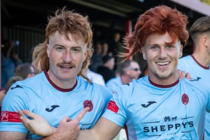 Taunton Town FC fans sport ginger mullet wigs in support of captain Tom Smith, sparking a booming trend at matches. The quirky craze has taken the club's home games by storm!