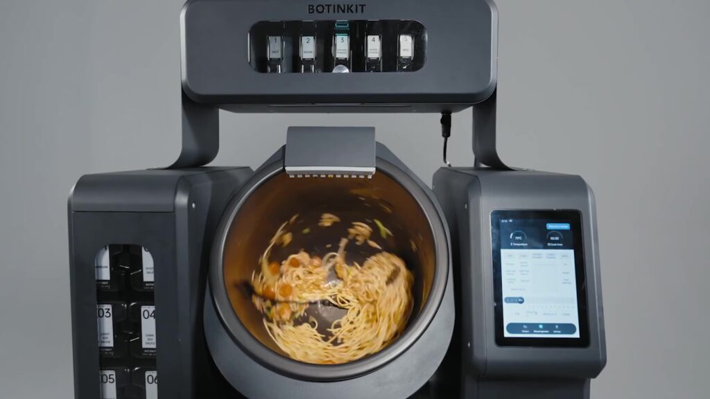 BOTINKIT's AI robot chef automates cooking tasks like stir-frying, boiling, and seasoning, aiming to cut restaurant costs by 30%. It offers precision, reducing waste and ensuring consistency.