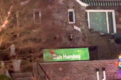 Bah Humbug! A real-life Scrooge in Dyker Heights, NYC, stands out with a dimly-lit home and a cheeky sign amidst dazzling Christmas displays.