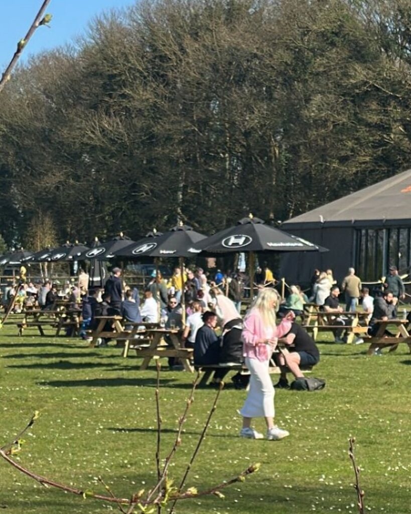 Jeremy Clarkson is facing backlash for charging £7.50 for a bacon roll and £14 for a burger without chips at his country pub, with critics calling the prices greedy.