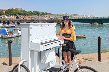 Musician Chloe Marie Aston is touring every UK town on her unique piano bike, bringing music and joy to streets nationwide with her dad by her side for the adventure.
