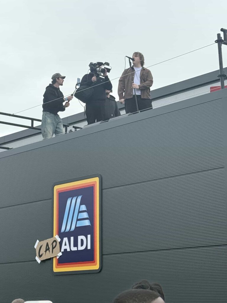 Lewis Capaldi surprises fans by performing his new single on the roof of an Aldi supermarket in Nottingham, leaving shoppers stunned by the unexpected rooftop gig.