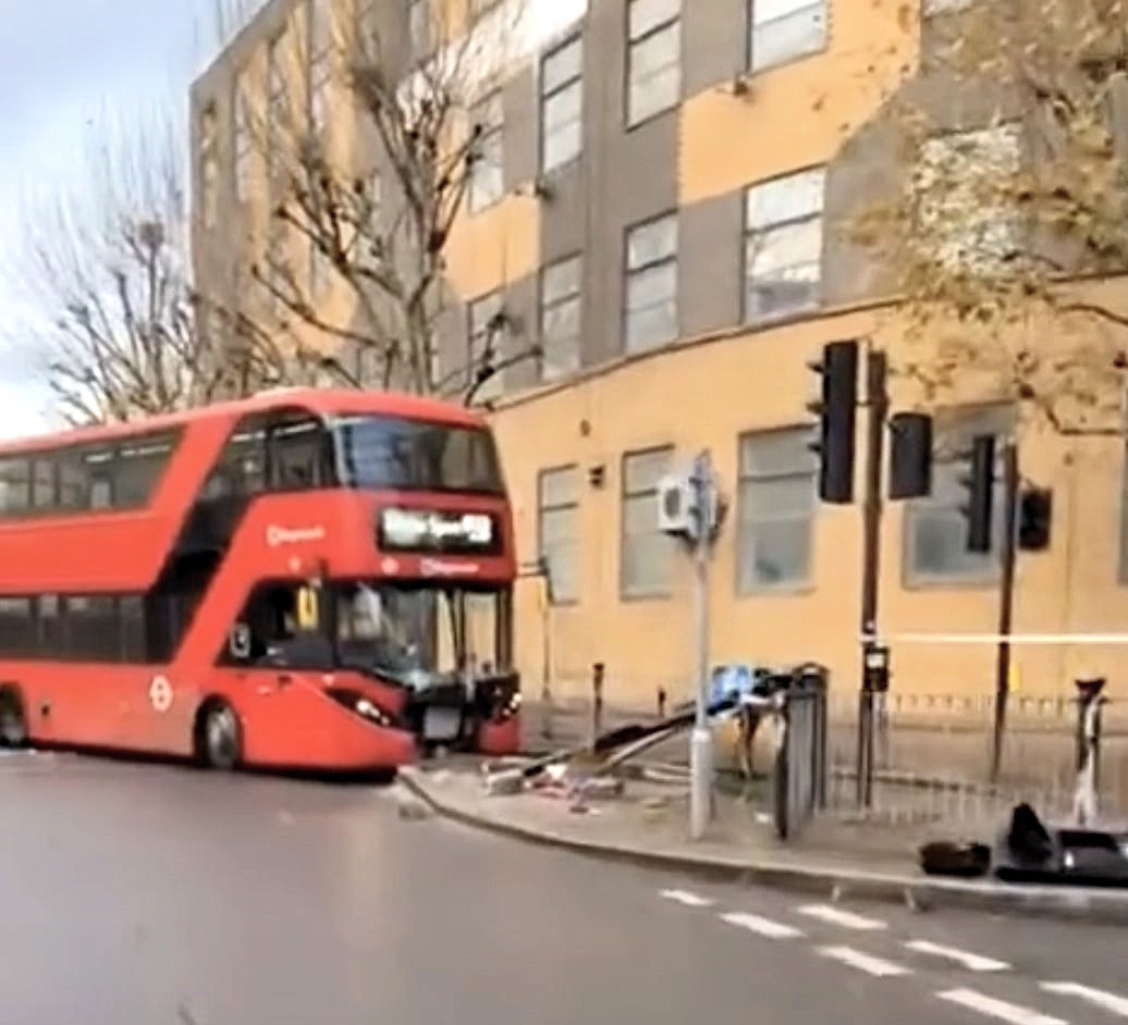 Double decker bus smashes into a bus lane sign in Docklands during rush hour leaving the front badly damaged as onlookers joke and a tow truck clears the road.
