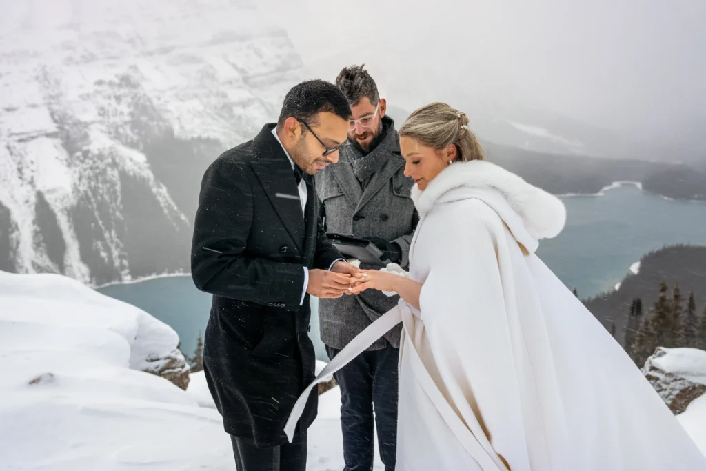 Couple braves a snowstorm to elope at Peyto Lake in Banff hiking in formalwear to say I do as stunning photos capture their windswept mountain wedding despite harsh conditions.