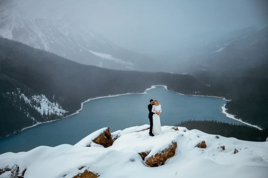 Couple braves a snowstorm to elope at Peyto Lake in Banff hiking in formalwear to say I do as stunning photos capture their windswept mountain wedding despite harsh conditions.