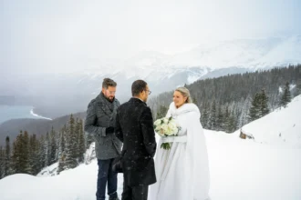 Couple braves a snowstorm to elope at Peyto Lake in Banff hiking in formalwear to say I do as stunning photos capture their windswept mountain wedding despite harsh conditions.