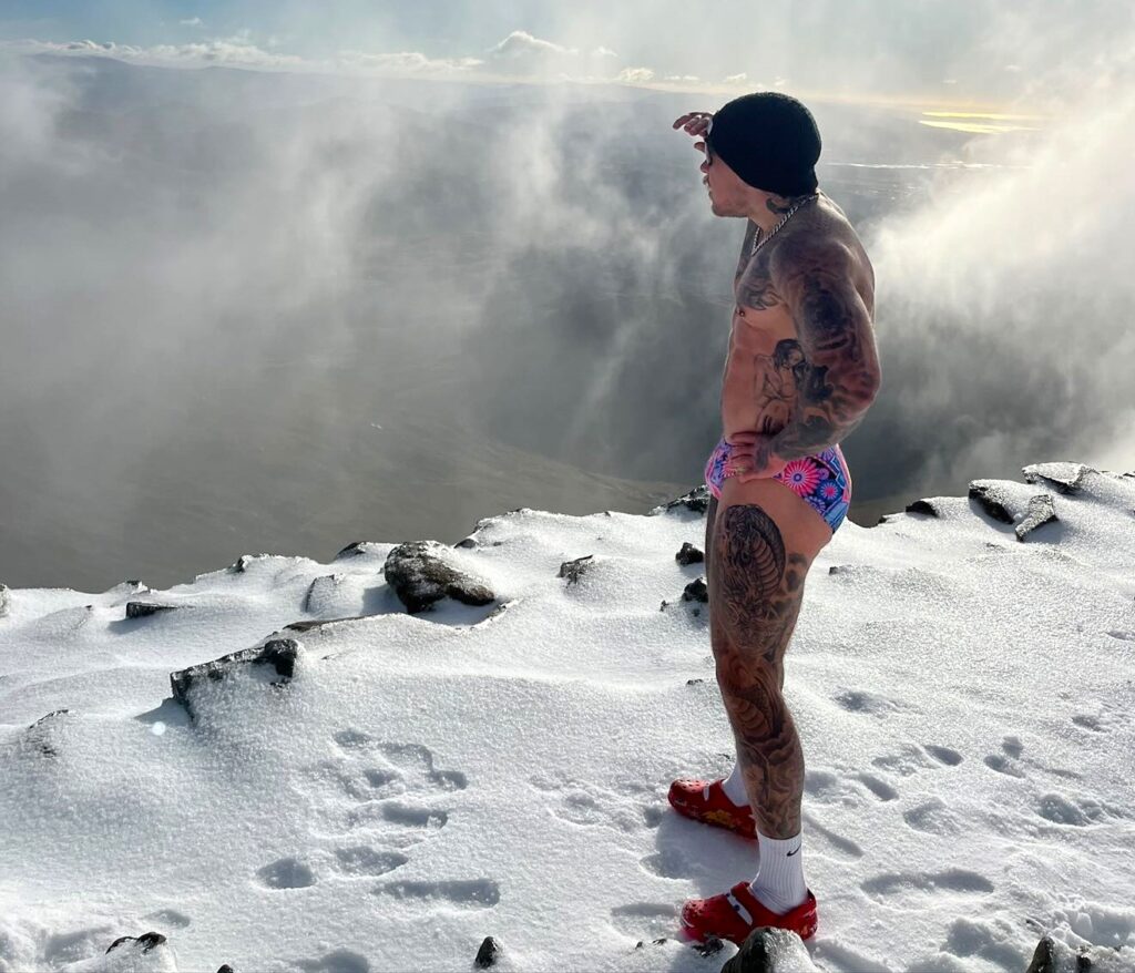 A British fitness coach stunned viewers by climbing Mount Snowdon in skimpy pants and Crocs battling snow and 40mph winds as part of a viral social media challenge.