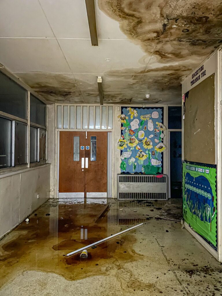 Urban explorer uncovers eerie abandoned primary school frozen in time since 2012, with ivy filled classrooms mouldy halls and grass growing indoors near Kent in darkness.
