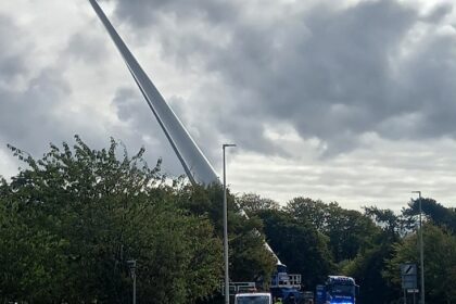 A towering 100 foot wind turbine blade amazes locals as it travels upright on a lorry through the Scottish Highlands showcasing the scale and spectacle of modern green energy projects.