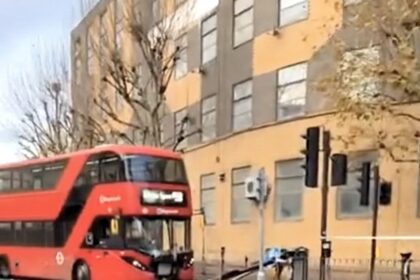 Double decker bus smashes into a bus lane sign in Docklands during rush hour leaving the front badly damaged as onlookers joke and a tow truck clears the road.