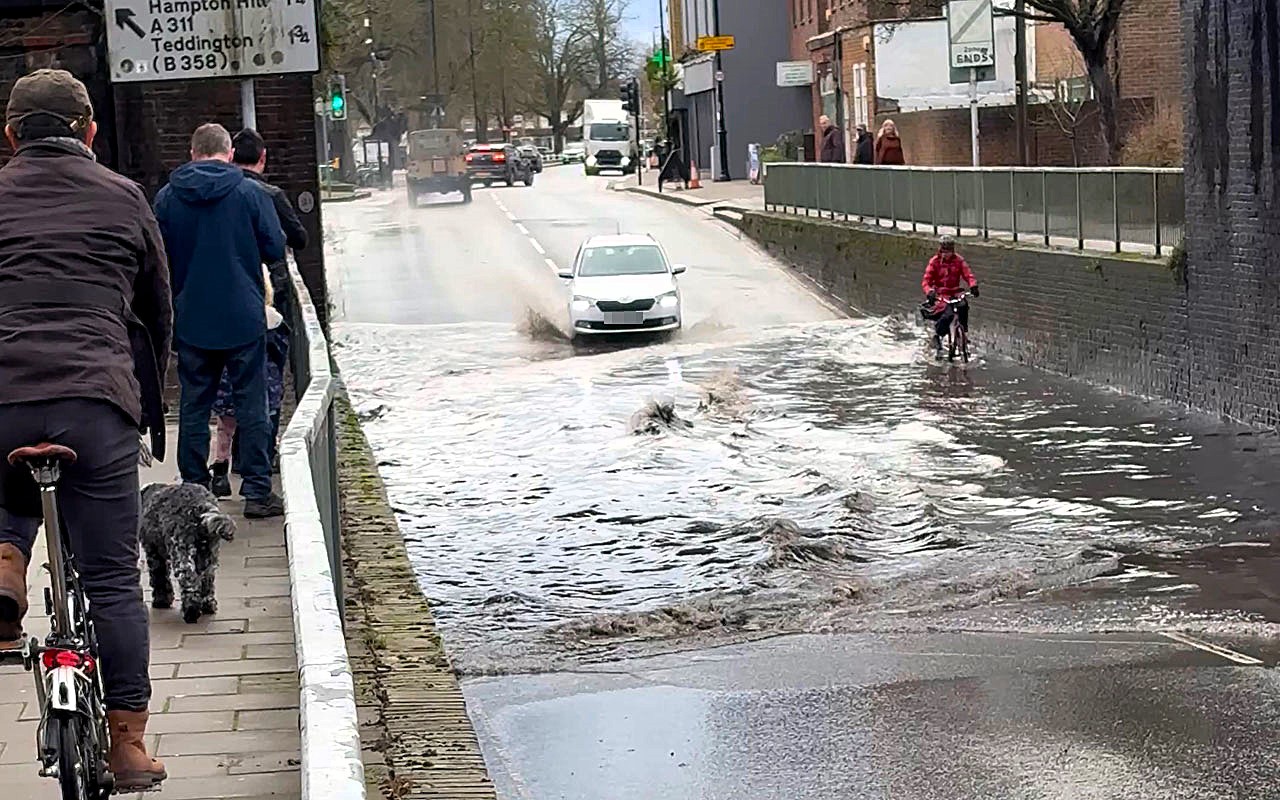A fearless cyclist pedalled through knee deep floodwater on Heath Road in Twickenham, unfazed even as a passing car sent waves crashing over her under a bridge