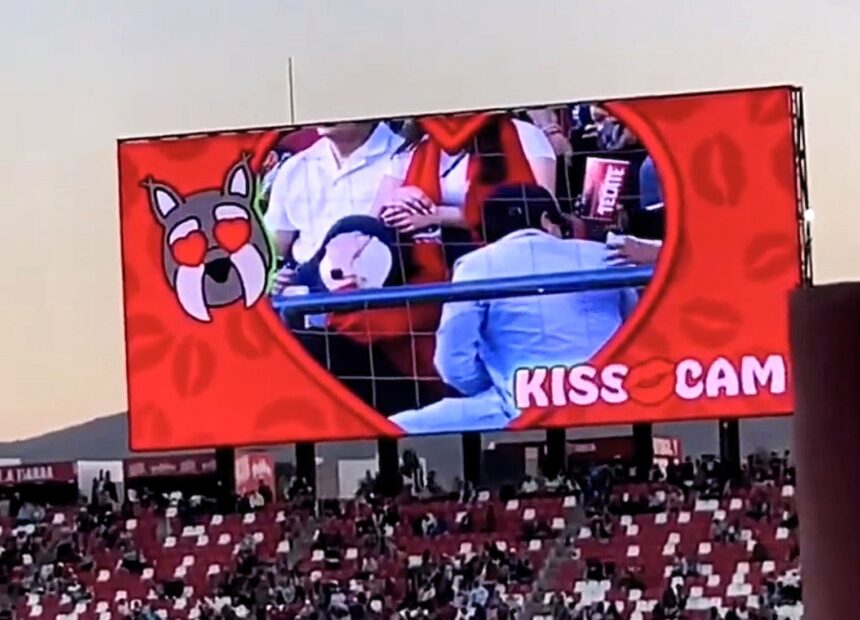 Couple caught on kiss cam at Mexican soccer match desperately hide faces as crowd jeers. Man turns 180 degrees away. Viral moment compared to Coldplay cheating scandal.