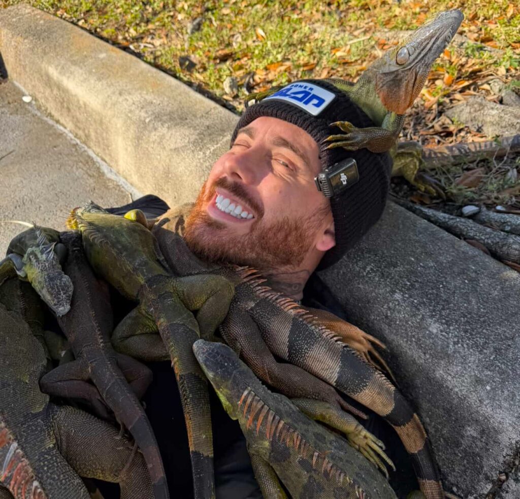 Influencer shocks viewers after covering himself with 100 iguanas to create a bizarre “iguana blanket” in a Florida car park, racking up millions of views online