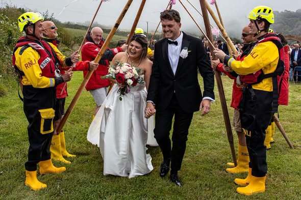 RNLI lifeboat crew surprised newlywed colleagues with a guard of honour made from gig boat oars and the charity's iconic yellow wellies after their Cornwall clifftop wedding.