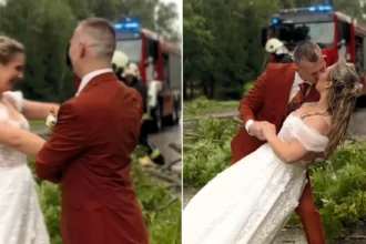 Bride and groom carry on with their wedding photos in a storm - dancing in the rain as firefighters clear a fallen tree from the road behind them.