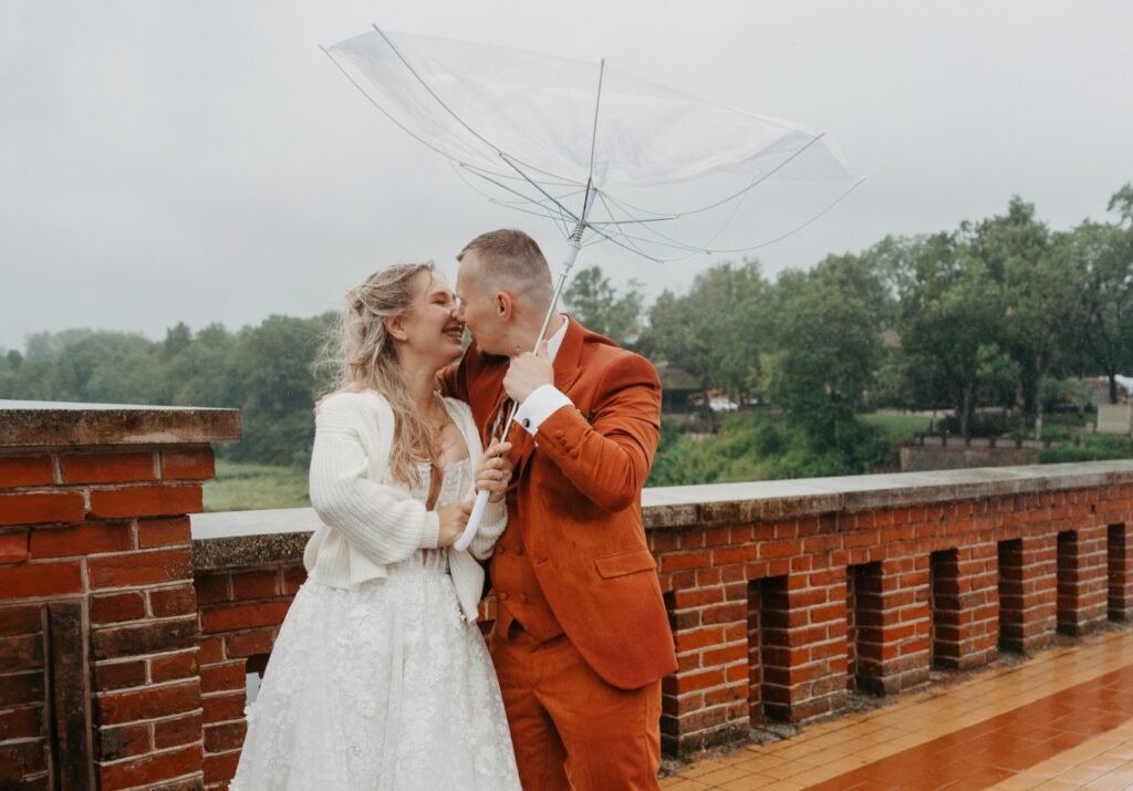 Bride and groom carry on with their wedding photos in a storm - dancing in the rain as firefighters clear a fallen tree from the road behind them.