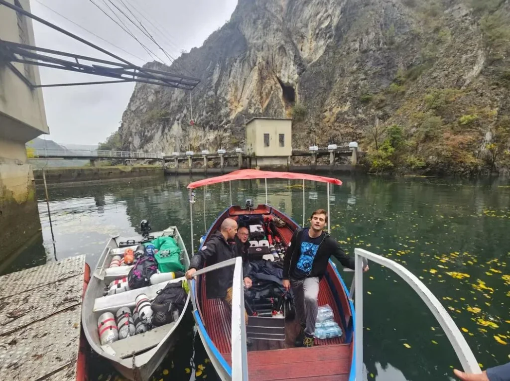 Diving team in speedboat approaching canyon with cave entrance.