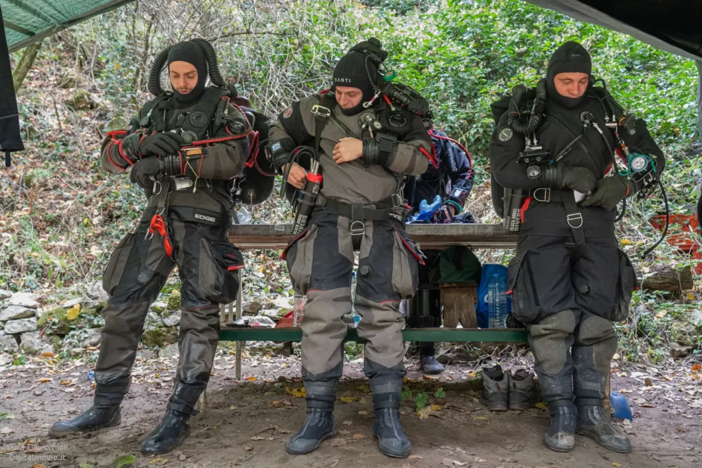 Three divers in full technical gear standing under helicopter.