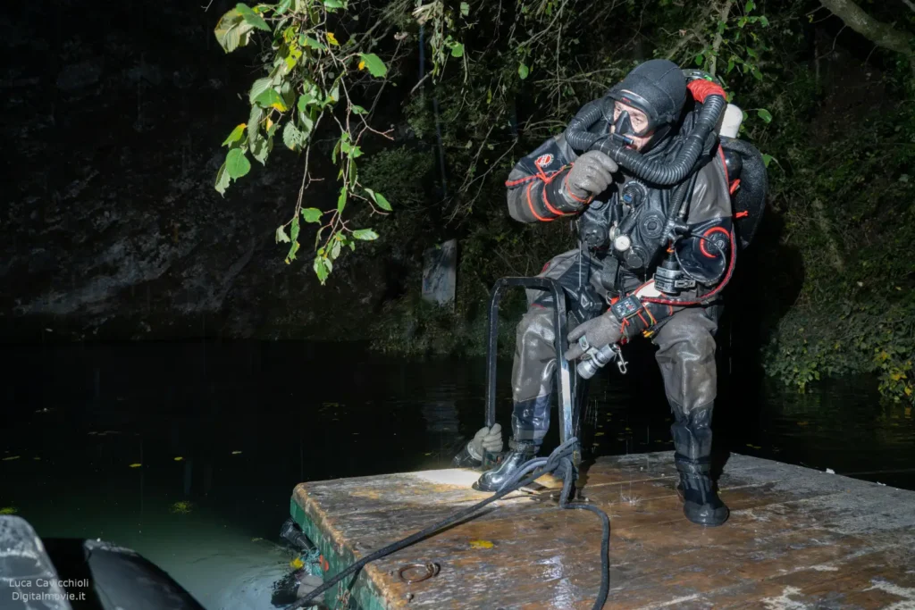 Diver in full technical diving gear preparing at cave entrance.