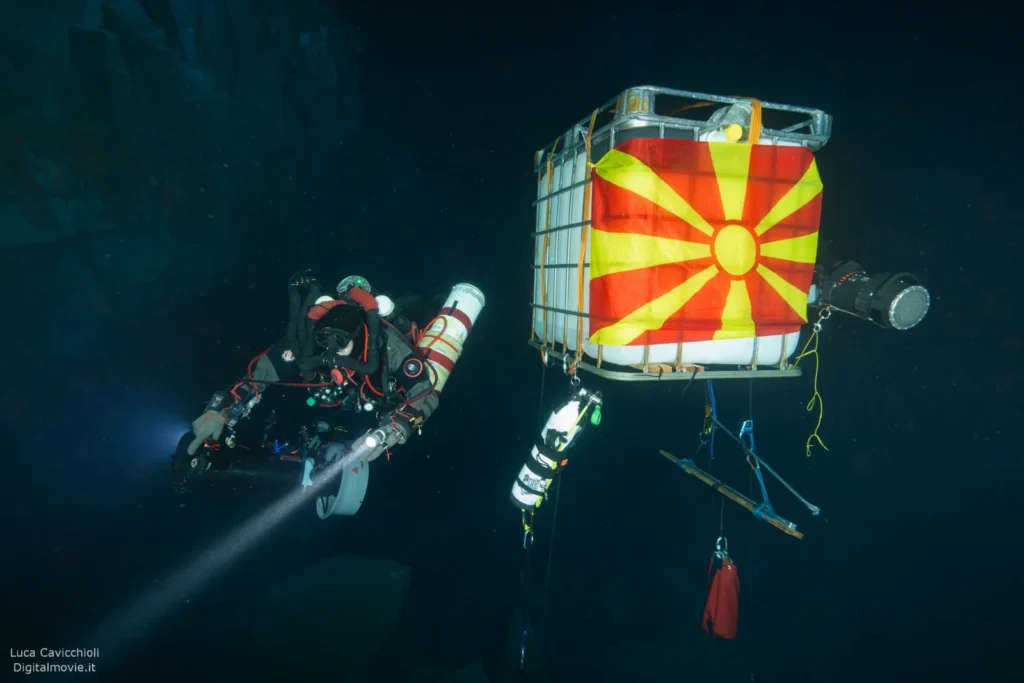Diver with Macedonian flag marker box deep underwater.