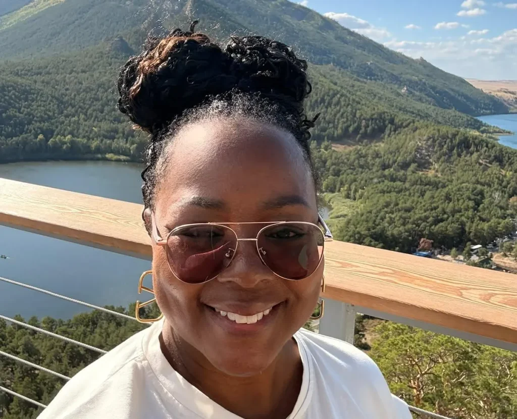 Tomiko Harvey wearing sunglasses in front of a mountain and lake.