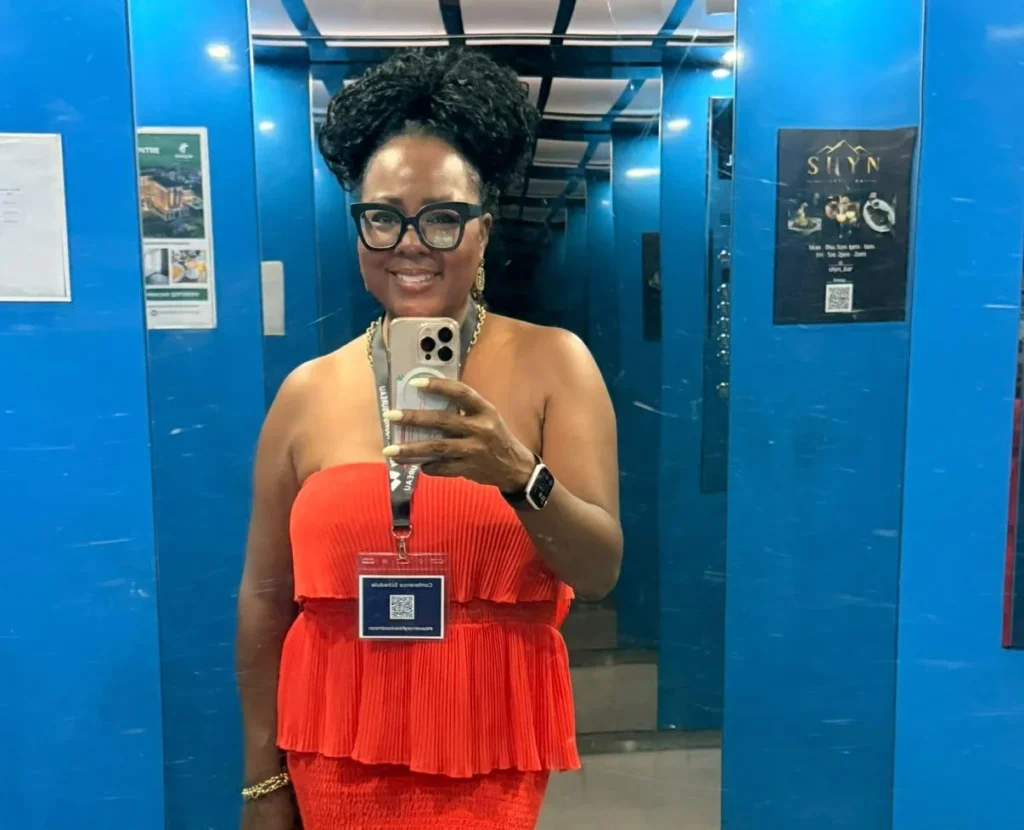 Tomiko Harvey in a red dress taking a mirror selfie in a lift.