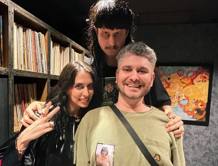 Three people posing together indoors near bookshelves.